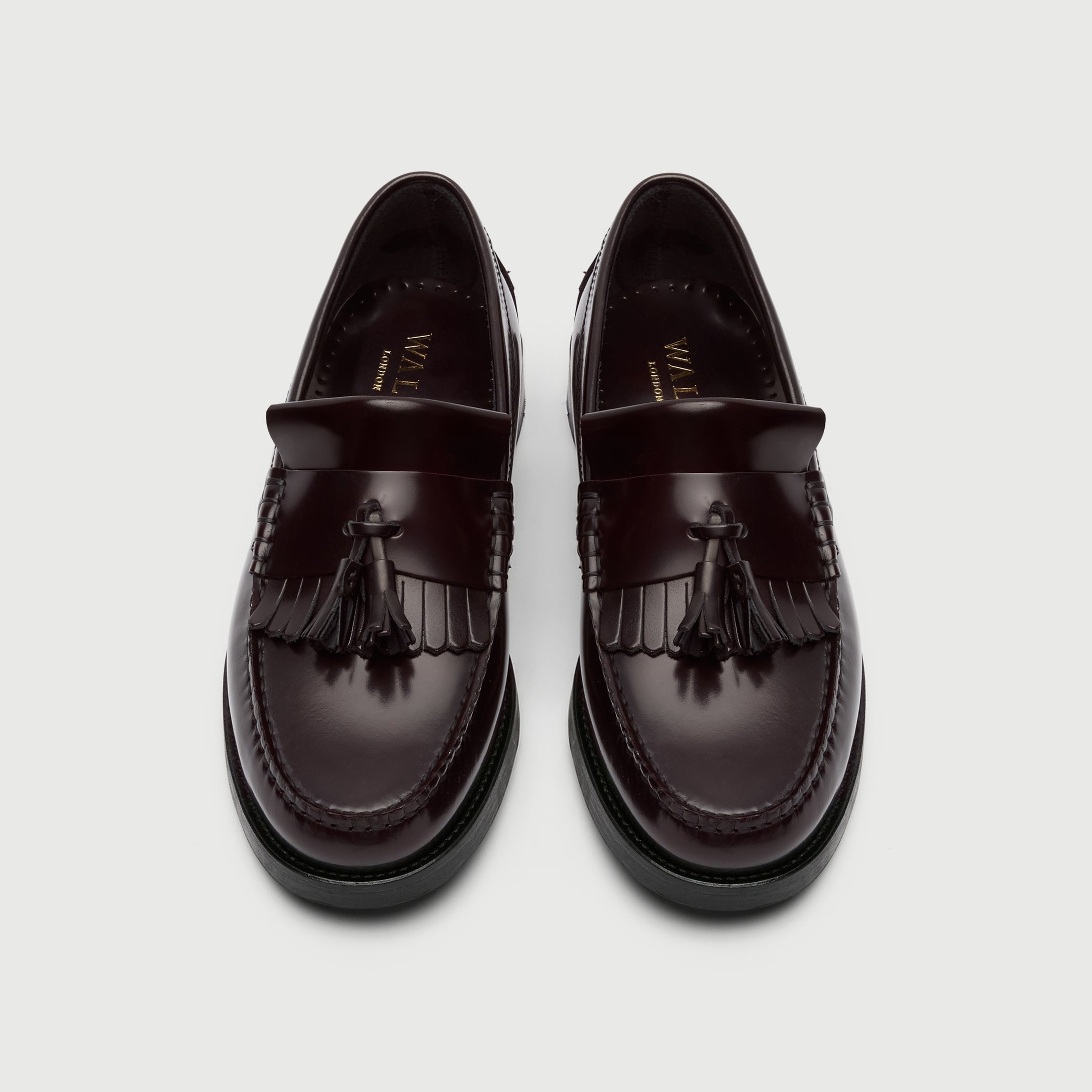Pair of dark brown loafers with tassels on a light gray background - Top View