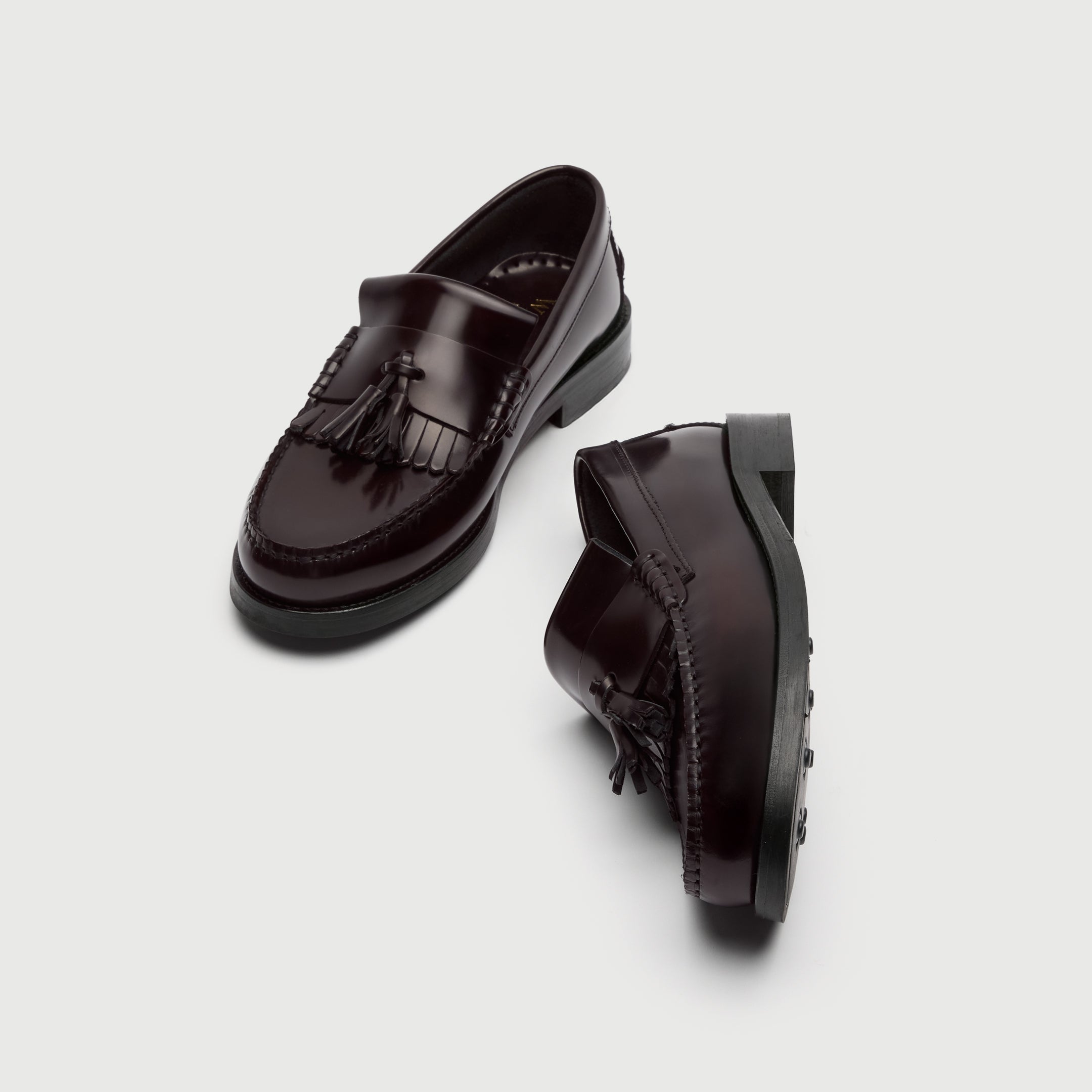 Pair of black loafers with tassels on a light gray background - Walk London Dalston Fringe Tassel Loafer Burgundy