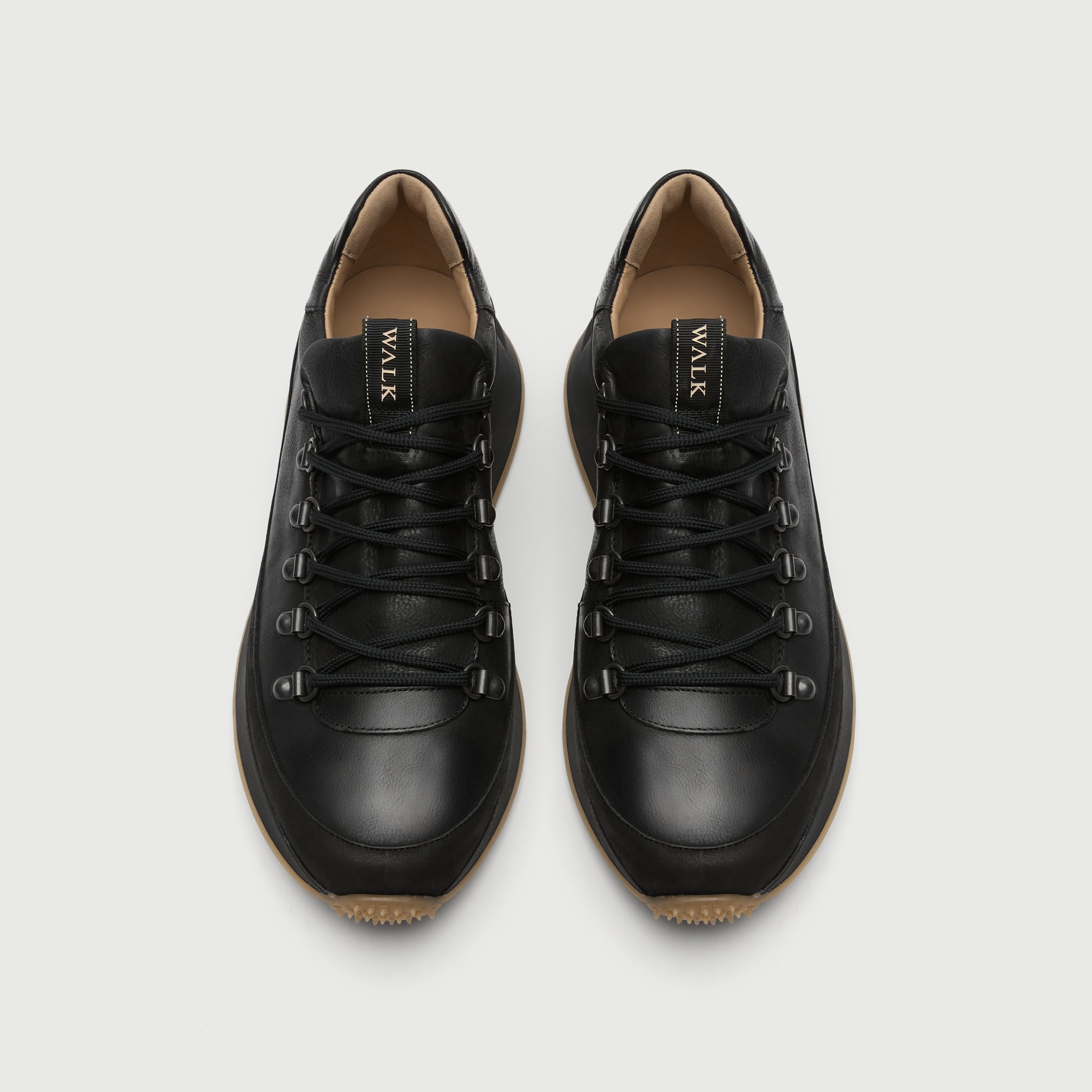 Pair of black leather sneakers on a light gray background. Walk London