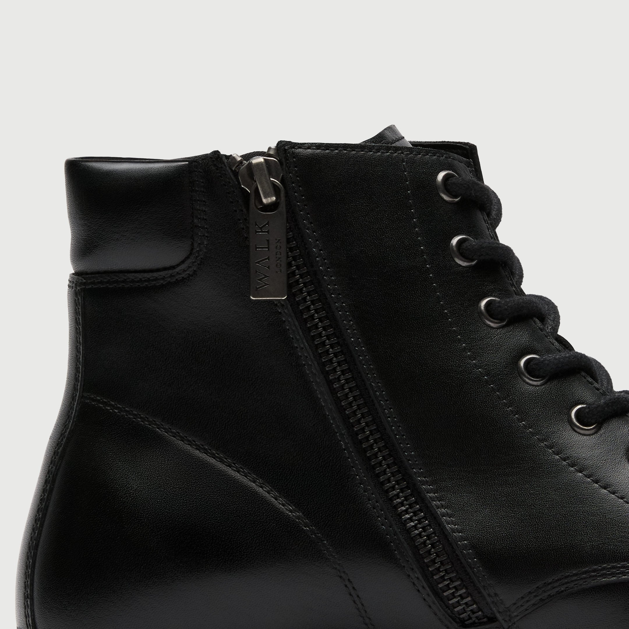 Close-up of a black leather boot with a zipper on a light gray background