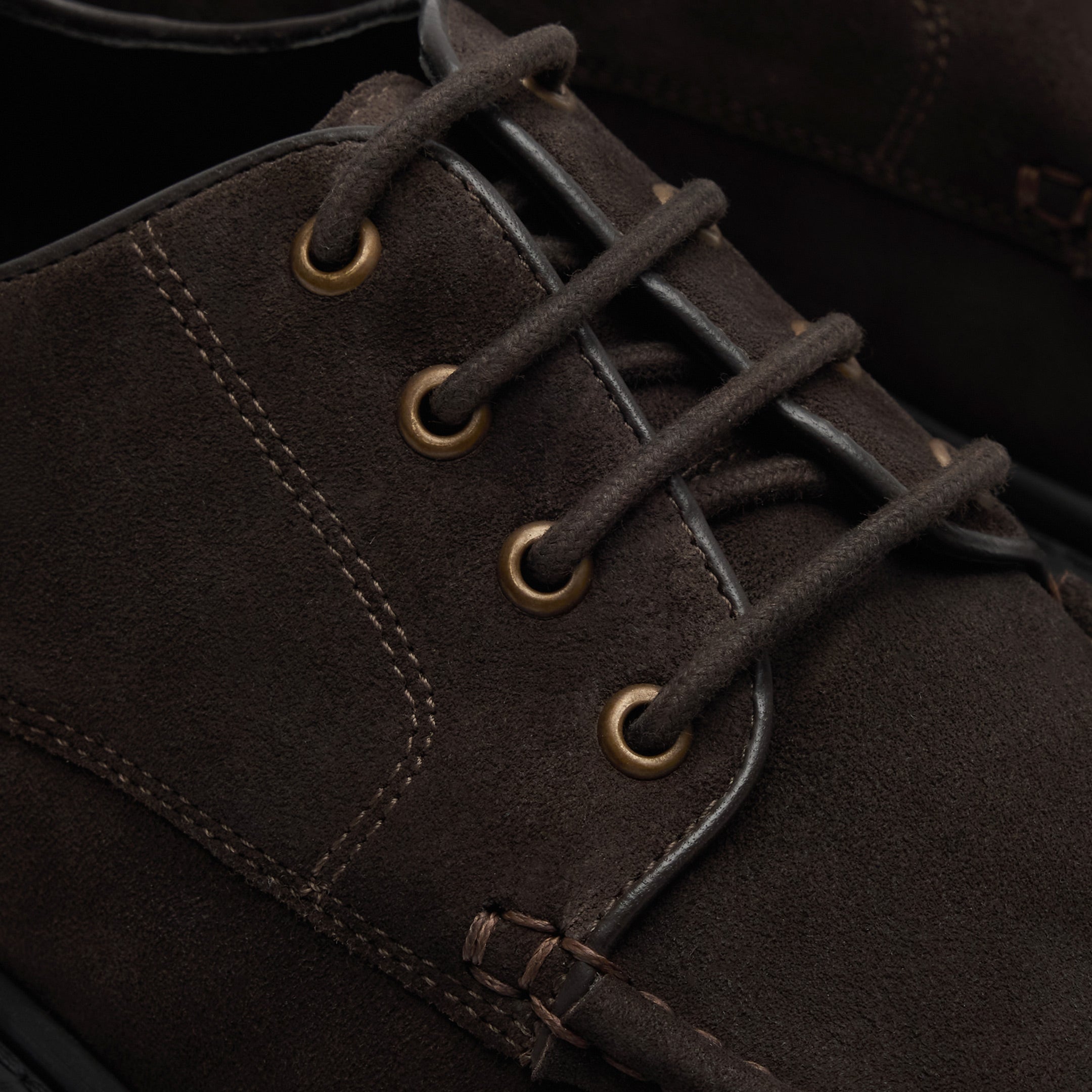 Walk London Hopper Lace Shoe in Brown Suede close up view of four brass toned eyelets with brown laces, stitch detailing, leather piping on edge