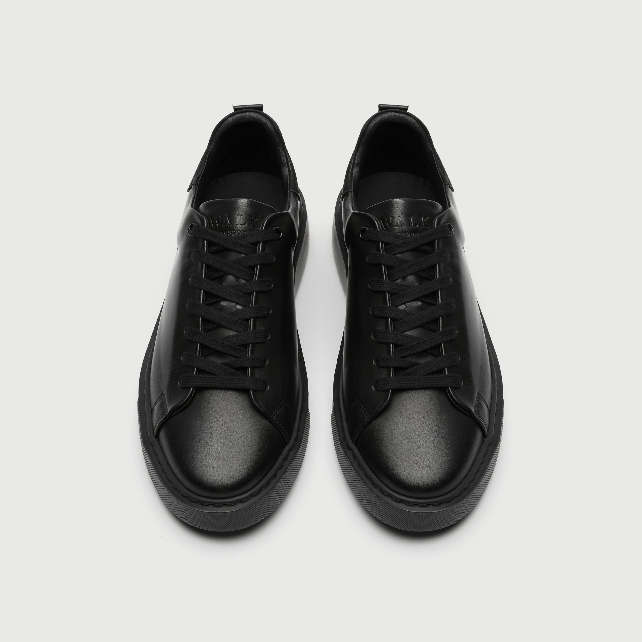 Pair of black sneakers on a light gray background - Walk London Pasadena Trainer in Black Leather top