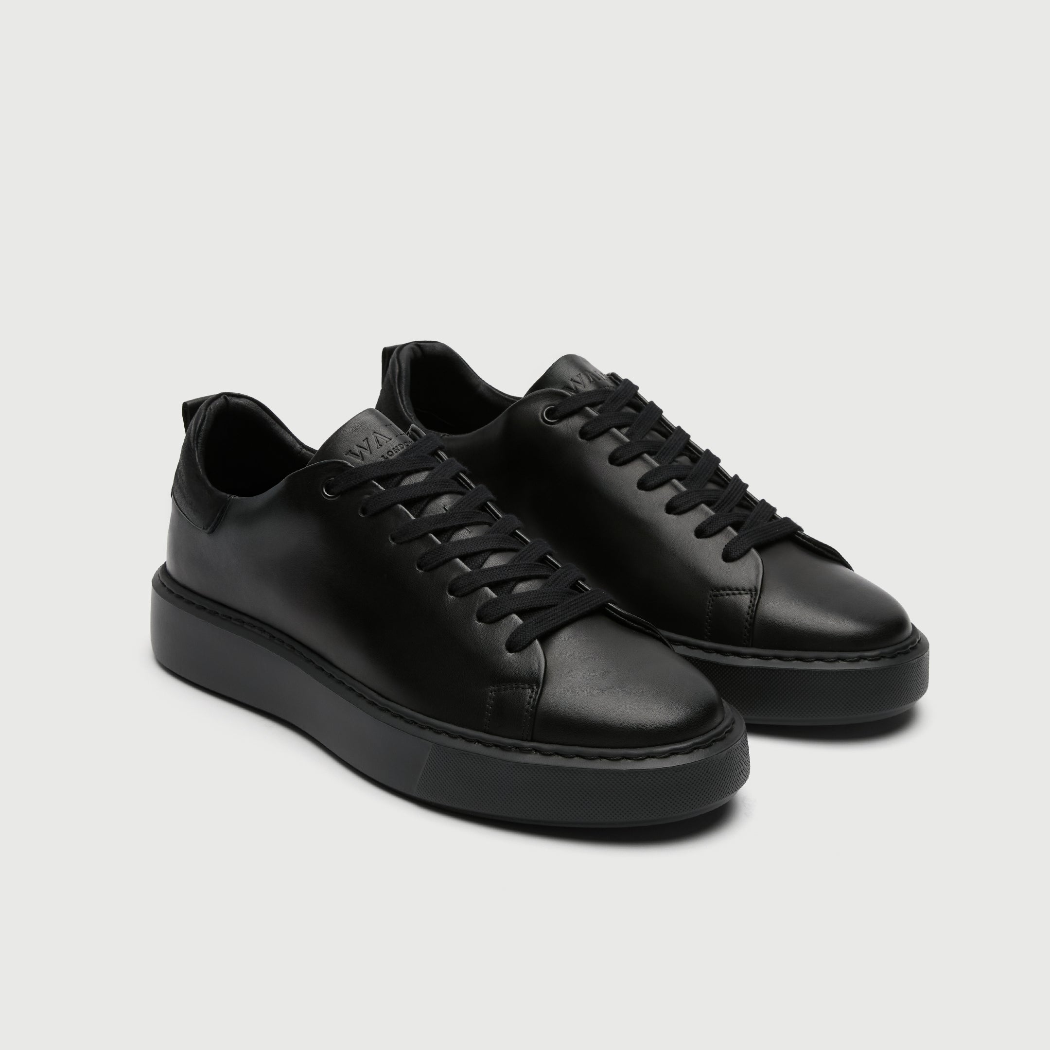 Pair of black leather sneakers on a light gray background - Walk London Pasadena Trainer in Black Leather