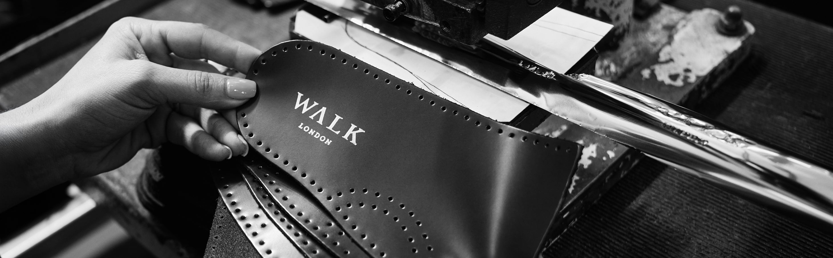 Black and white photo of hand holding leather insoles with Walk London foil branding as they are being made in the factory