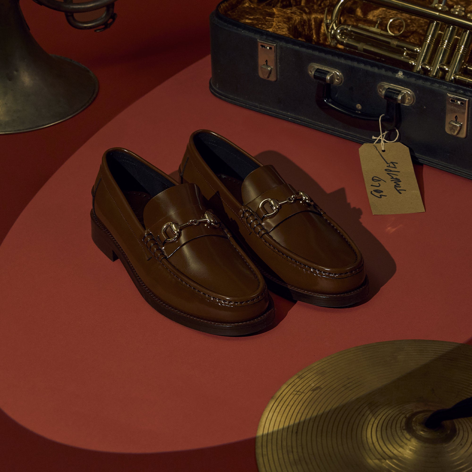 Mens brown trim loafers on red background with musical instruments