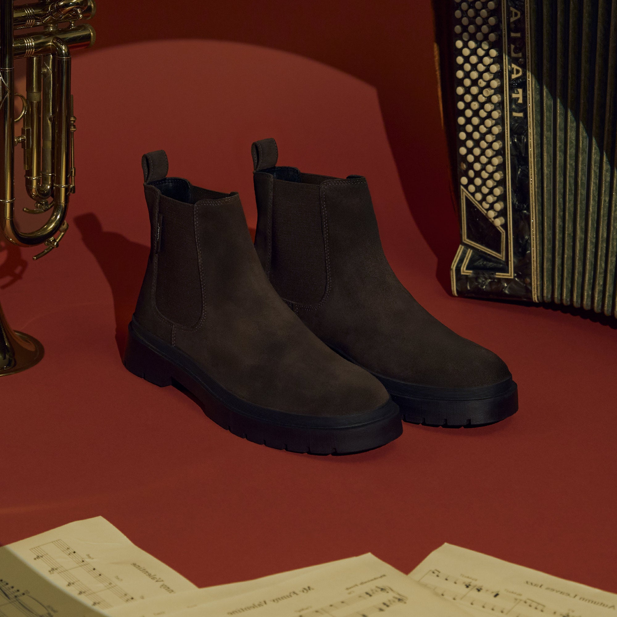 Mens brown suede chelsea boots on red background with sheet music and instruments