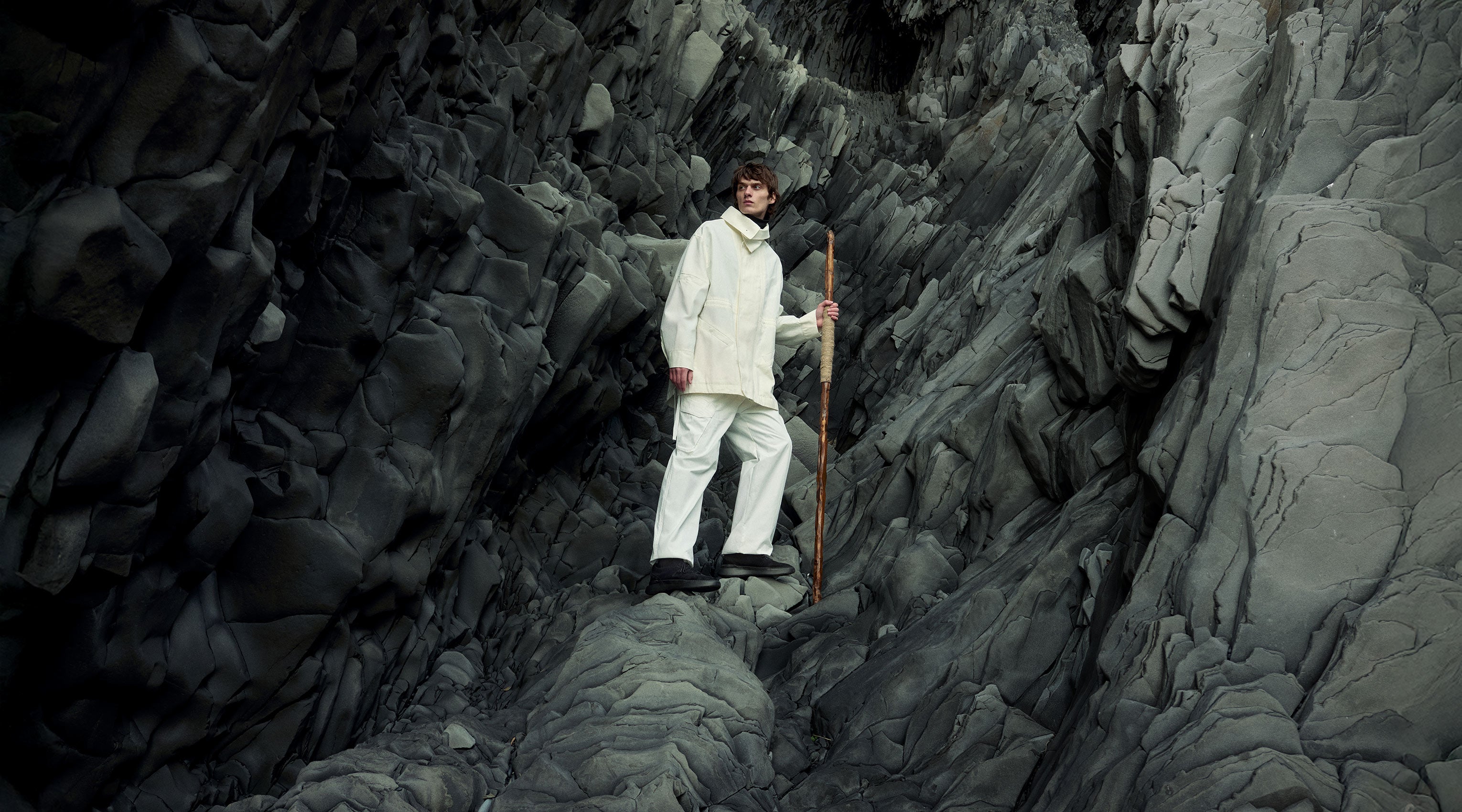 Man in white clothes with black trainers on rocky cliff