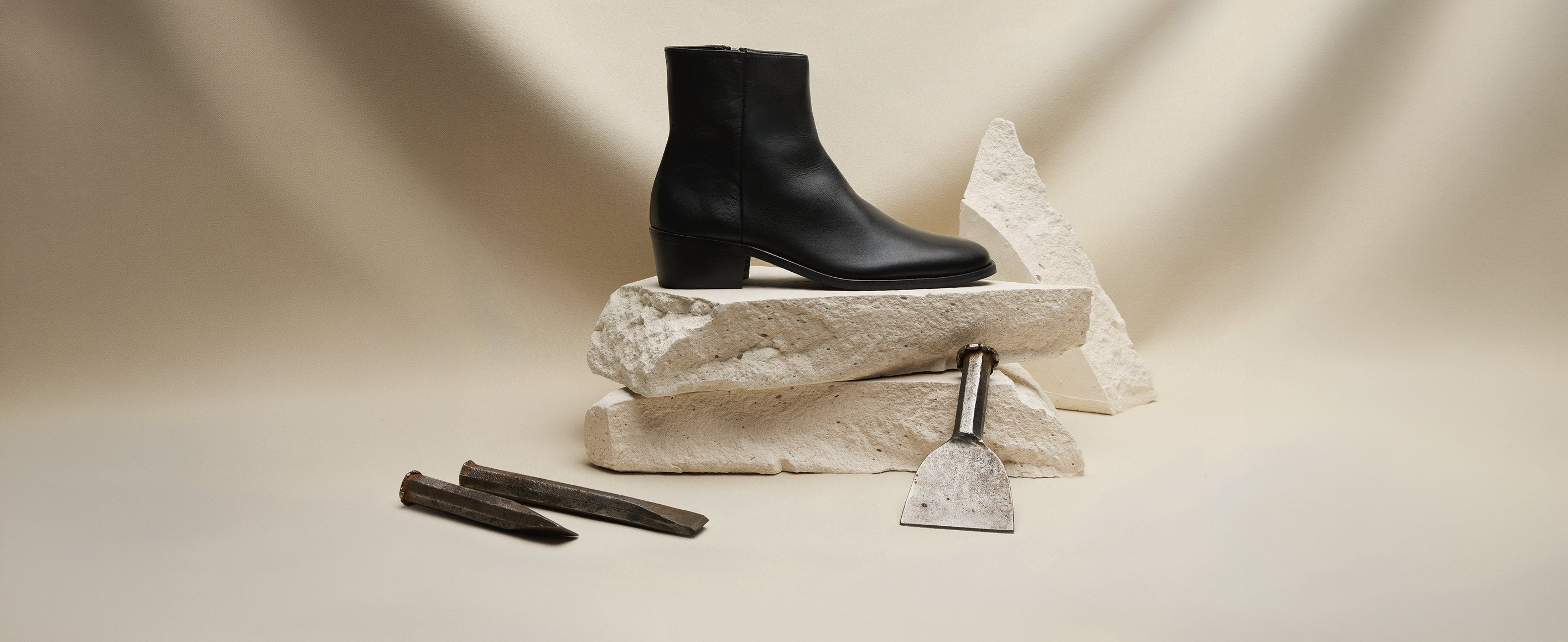 Hoxton black leather cuban heel boots balanced on white stone slabs with stone masonry tools on a cream background