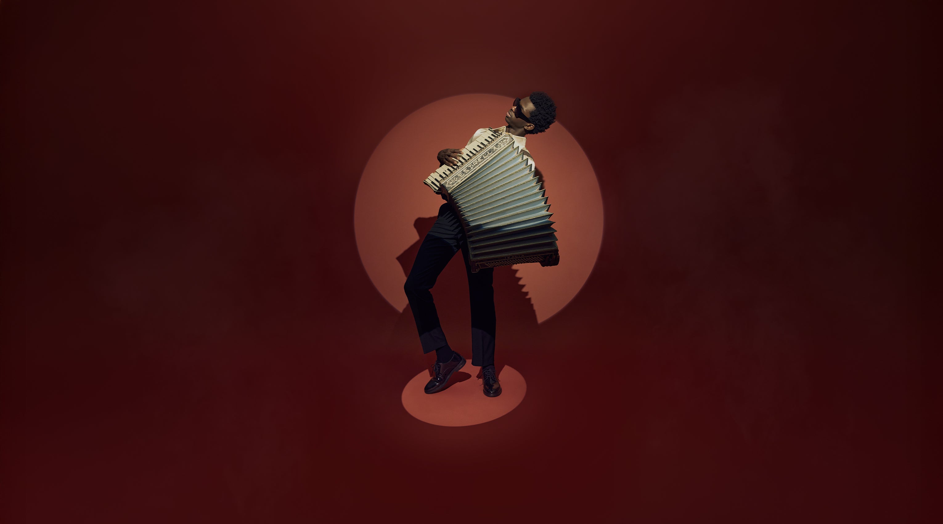 Person playing an accordion against a red background wearing black shoes