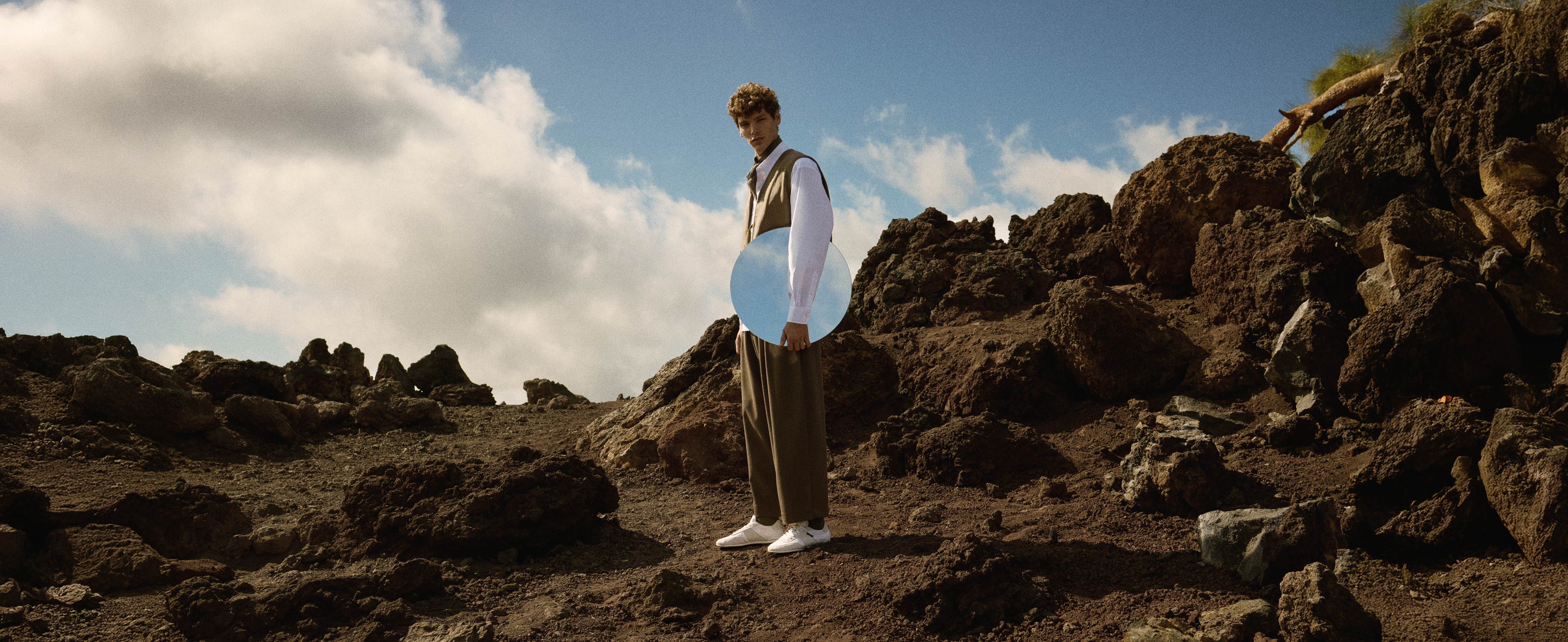 Man standing on a rocky landscape wearing white trainers with a blue sky and clouds