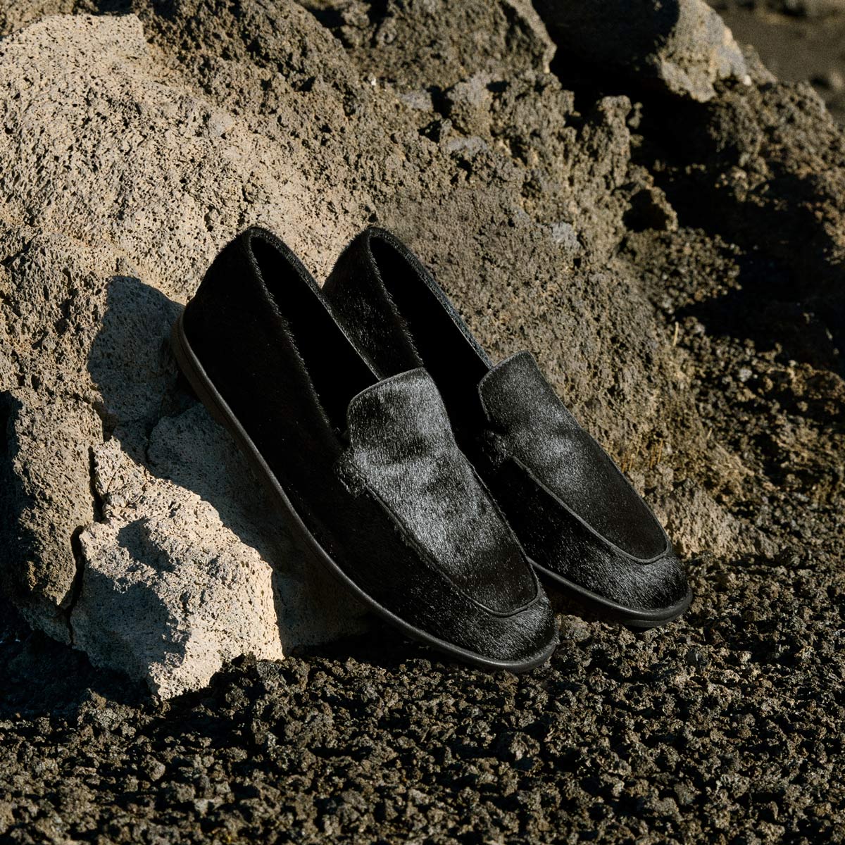 Walk London San Marino Men's Black Pony Hair Loafers leaning on rocky background