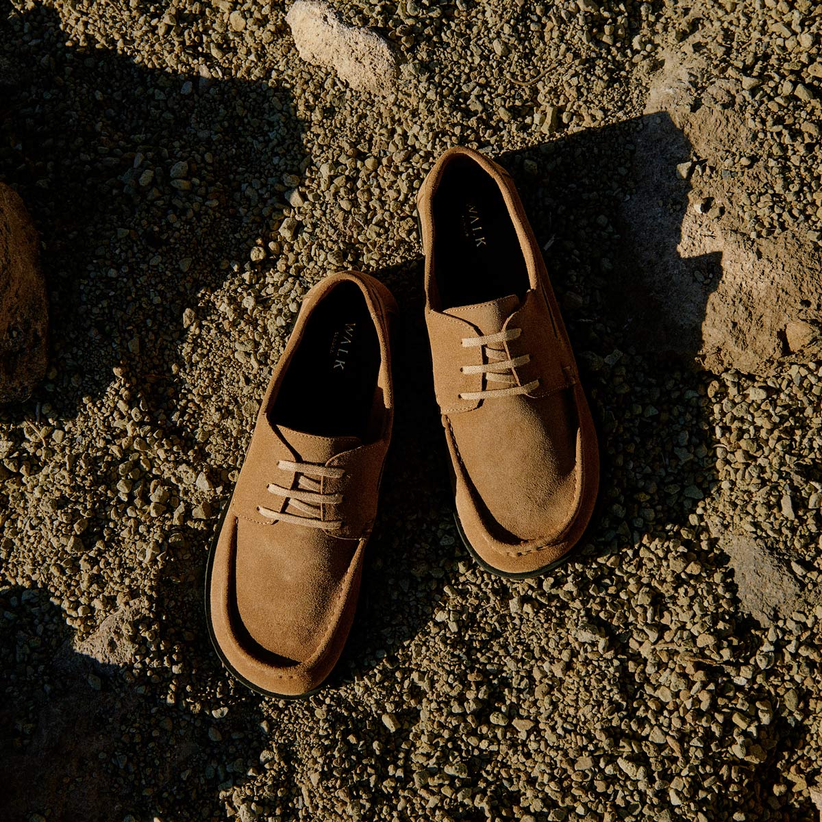 Walk London Roma Men's Boat Shoe in tan suede on beige sandy and rocky background