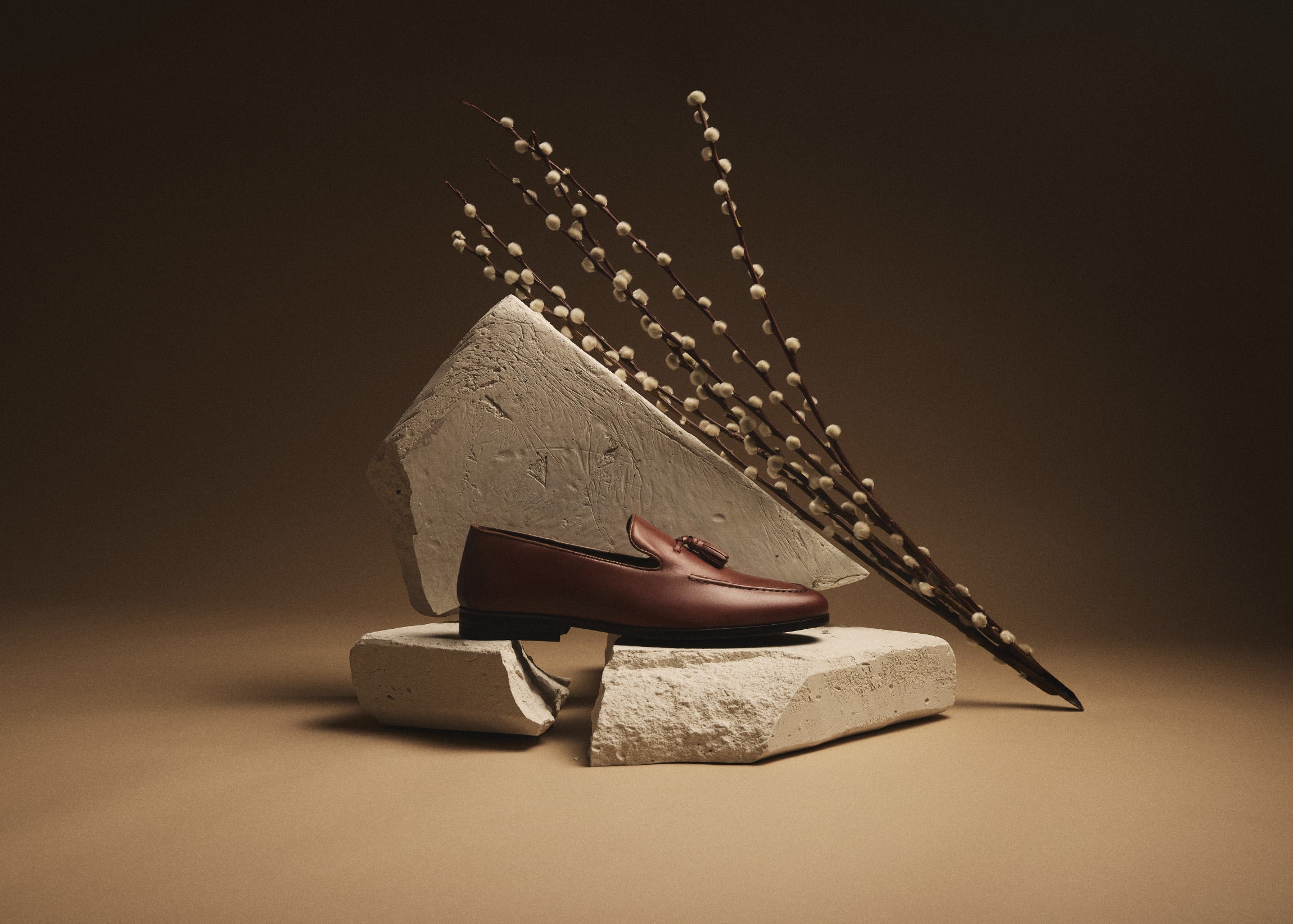 Tan Ischia Tassel Loafer men's wedding shoe resting on white stone with white catkins branch