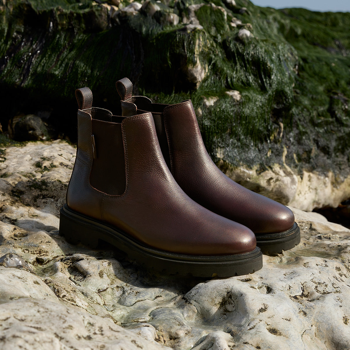 Hackney mens brown leather Chelsea boots on light coloured rock covered with seaweed