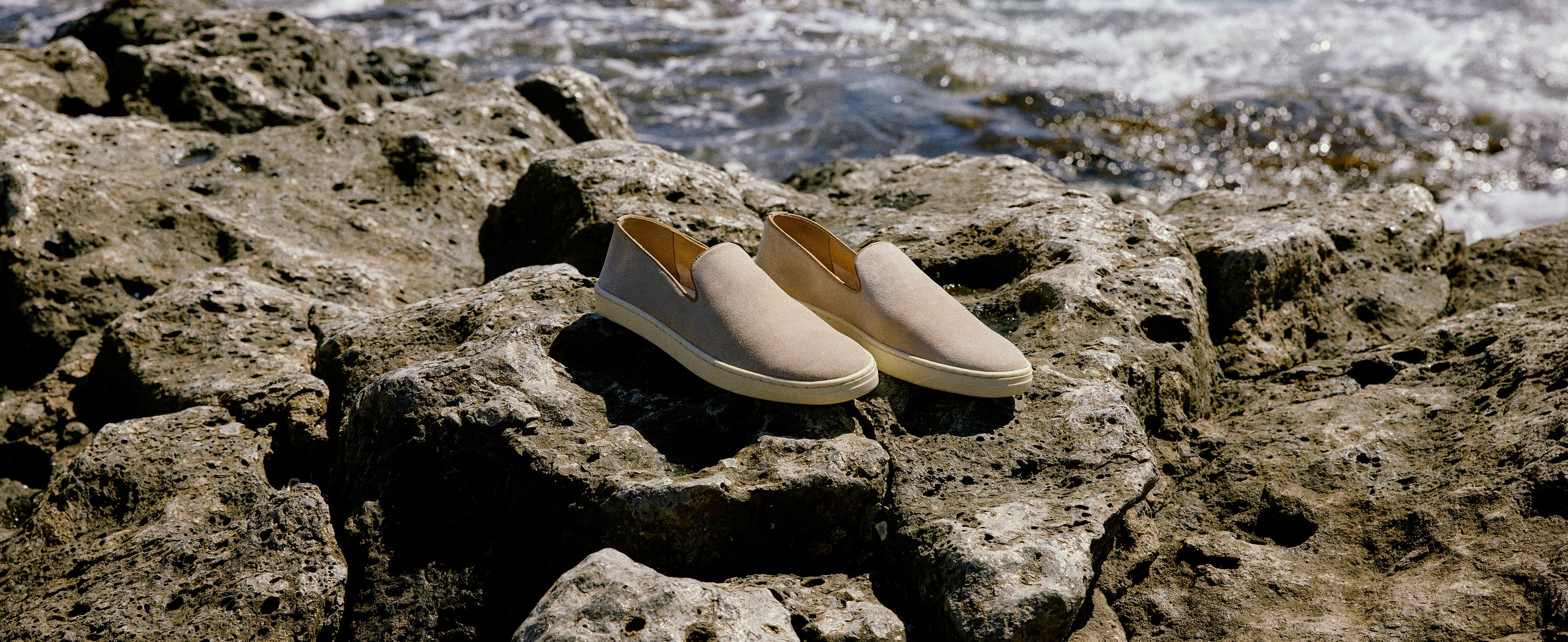 Pair of Palermo mens stone suede slip on shoes sitting on rocks by the sea