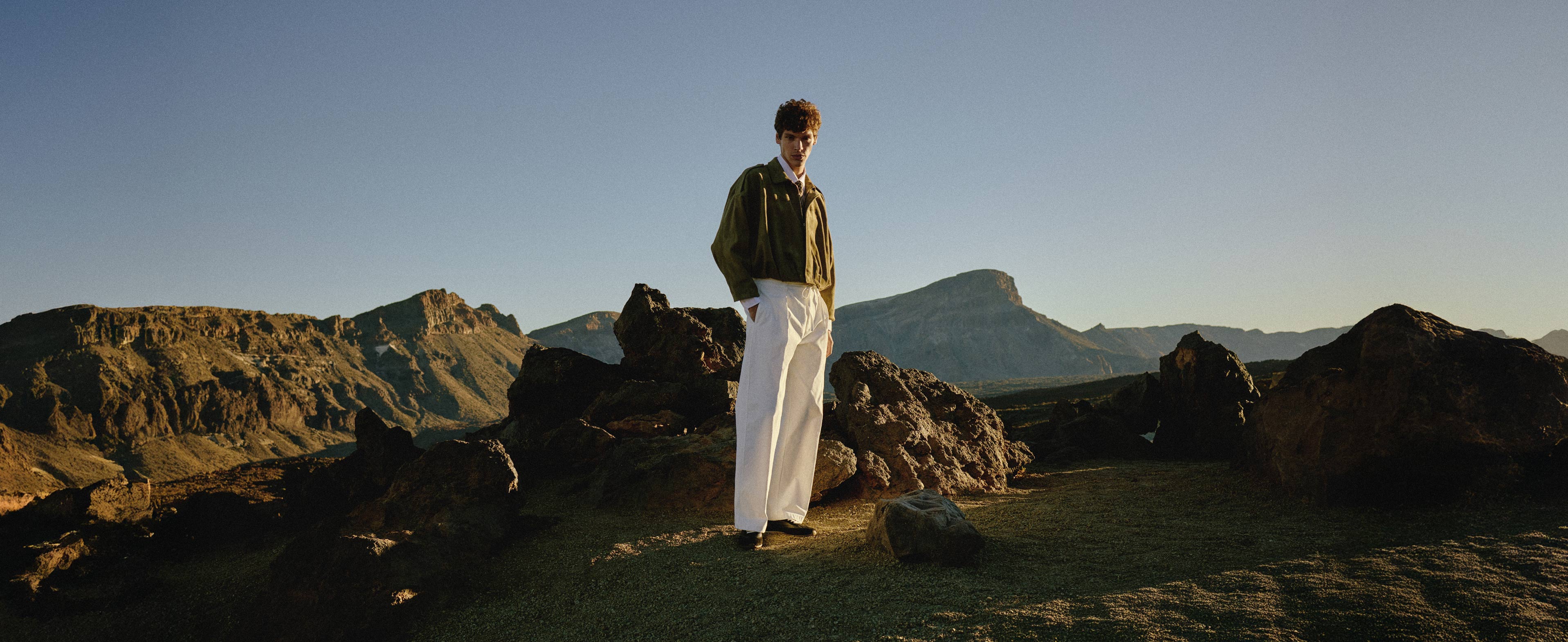 Man stood in rocky landscape wearing green jacket, white trousers and Bologna leather trainers in black