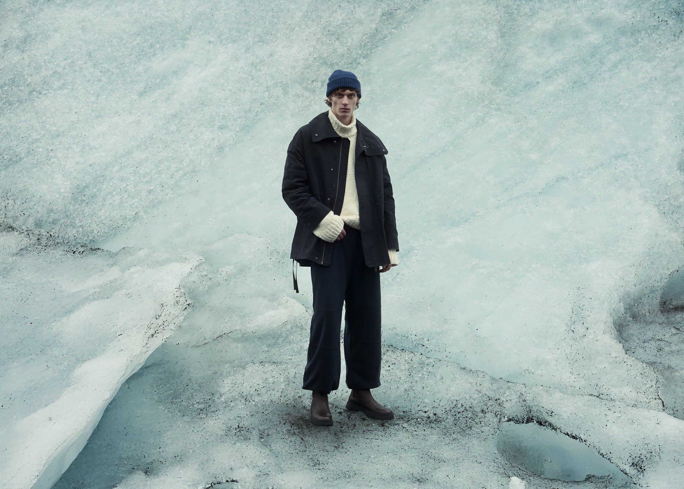 man wearing winter clothes and brown leather boots stood on glacier