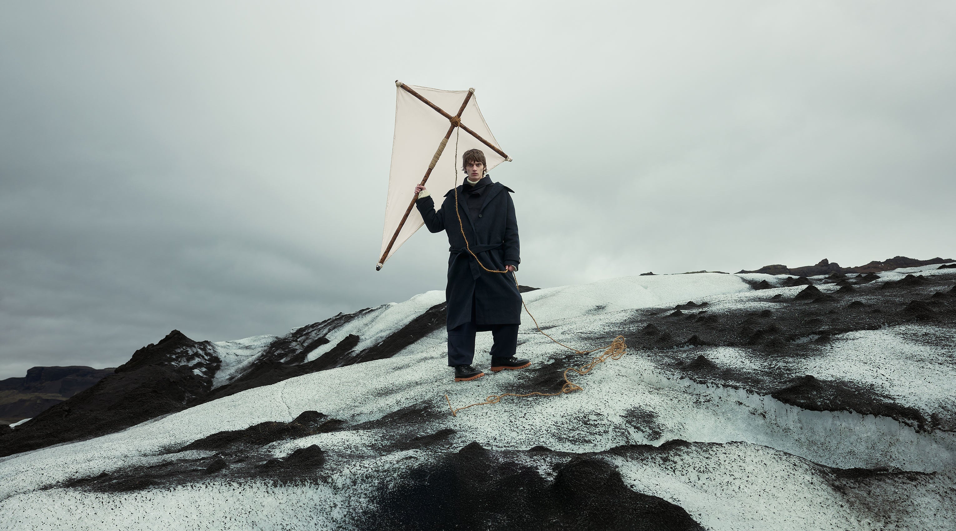 man stood on glacier holding kite wearing black boots - discover winter collection