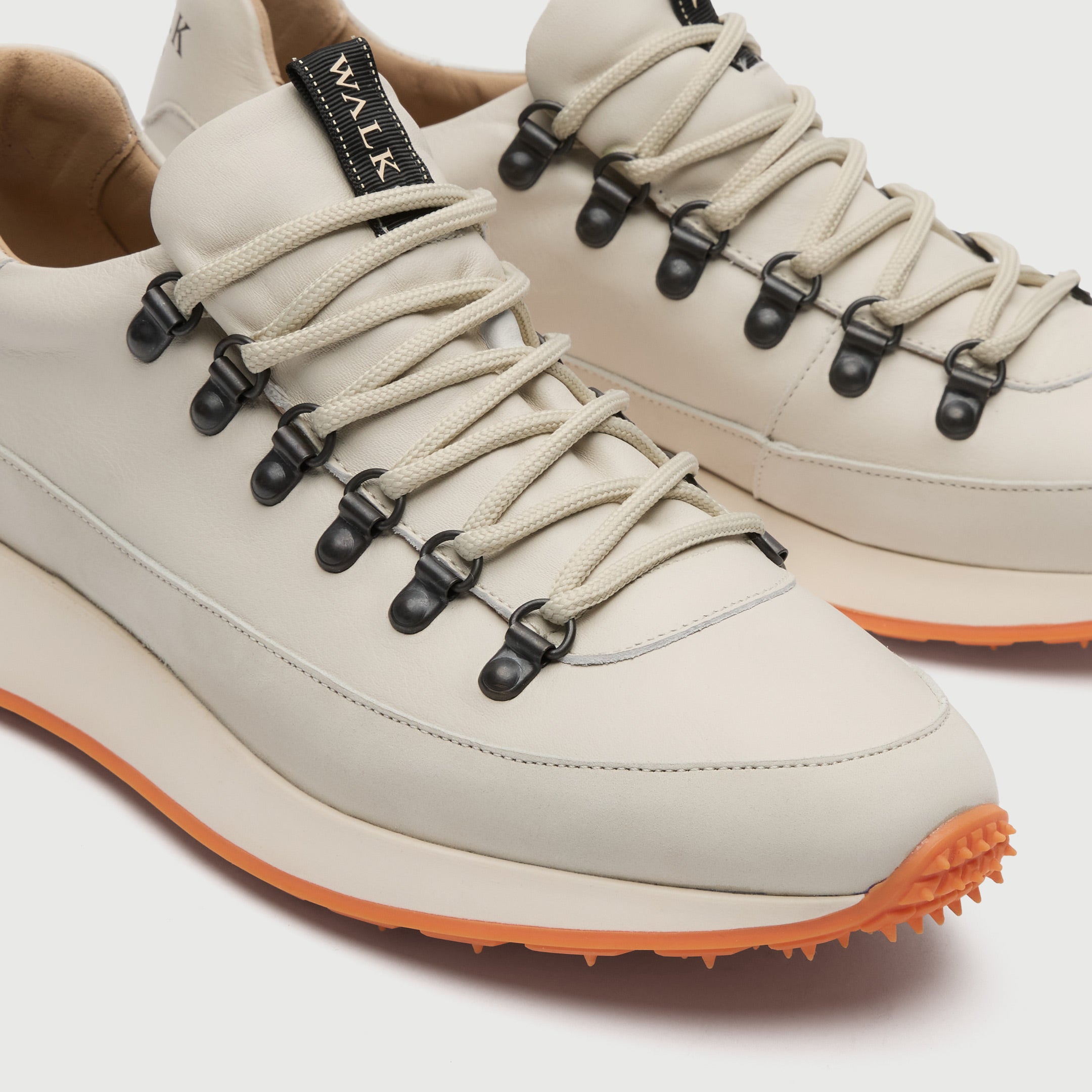 Close up view of a Walk London Hampstead Hiking Trainer with an orange sole on a light grey background